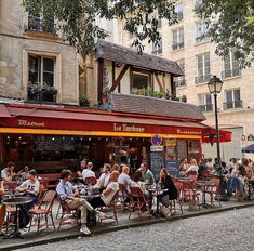 people sitting at tables in front of a restaurant with red awnings on the street