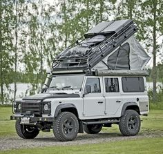 an off - road vehicle with a tent on the roof is parked in front of some trees