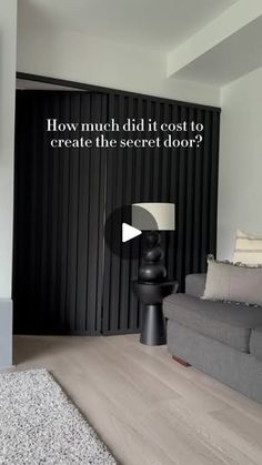 a living room with a grey couch and white rug on the floor next to a black wall that says how much did it cost to create the secret door?