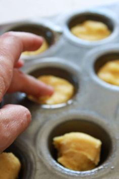 a hand reaching into a muffin tin filled with cupcake batter