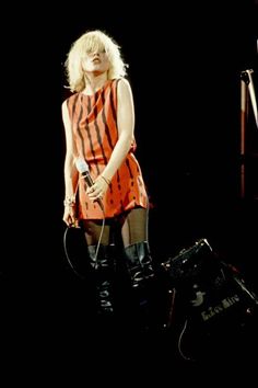 a woman in an orange and black striped dress holding a microphone while standing on stage