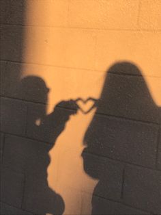 the shadow of two people standing next to each other with their hands in the shape of a heart