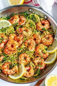 shrimp and zucchini pasta in a pan with lemon wedges