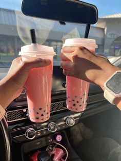 two people holding pink drinks in their hands while sitting in a car with the steering wheel behind them