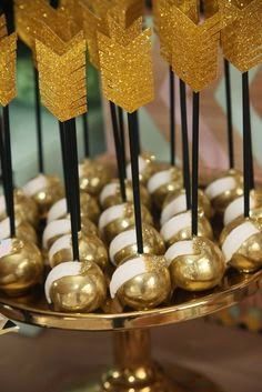 gold and white candies are on a plate with black sticks sticking out of them