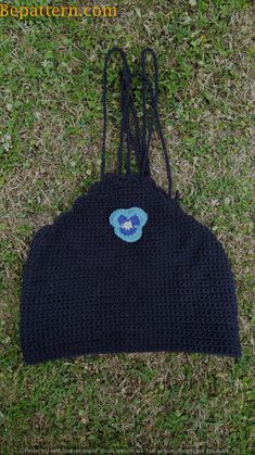 a black crocheted hat with a blue flower on it sitting in the grass