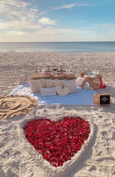 a heart - shaped bed on the beach with pillows and other items laid out in the sand