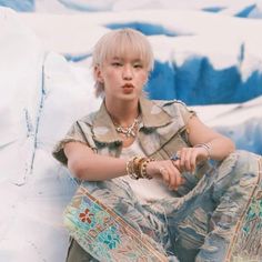 a young woman sitting on top of a snow covered mountain with her hands in her pockets