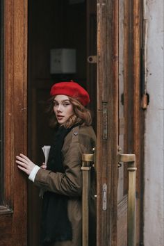 a woman in a red hat and coat is standing at the entrance to a building