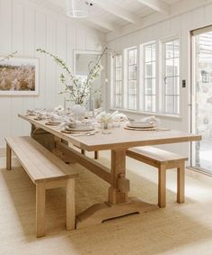 a dining room table set with place settings and flowers in vases on the side