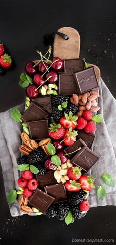 an assortment of chocolates, fruit and nuts arranged on a towel with some green leaves