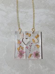 a necklace with flowers and hearts in it on a silver chain that is attached to a glass block