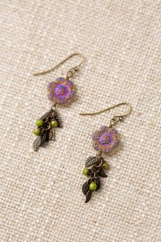 two pairs of earrings with beads and leaves hanging from them on a piece of fabric