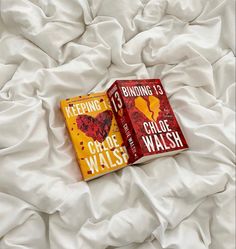 two books sitting on top of a bed next to each other in front of white sheets