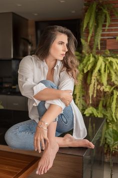 a woman sitting on top of a wooden table in front of a potted plant