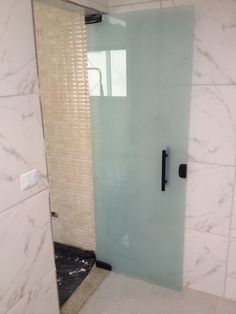 a glass shower door in a bathroom with white marble walls and floor tiles on the wall