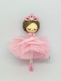 a doll with a pink tutu and tiara is posed on a white surface