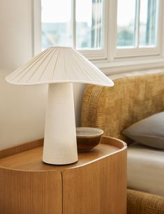 a white lamp sitting on top of a wooden table next to a bed in a room