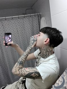 a man with tattoos taking a selfie in the bathroom while on his cell phone