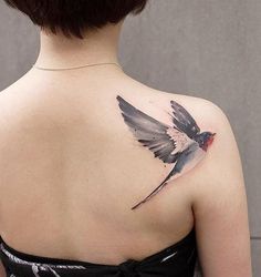 the back of a woman's shoulder with a bird tattoo on it