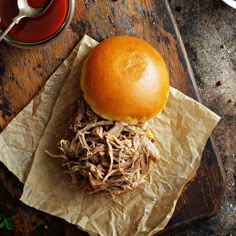 a pulled pork sandwich sitting on top of a wooden cutting board