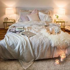 a bed with white blankets and pillows next to two small candles on the floor in front of it