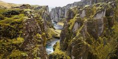 a river flowing through a canyon surrounded by tall rocks and moss covered mountains in iceland