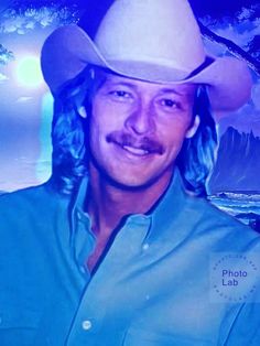 a man with long hair wearing a cowboy hat in front of a mountain and lake