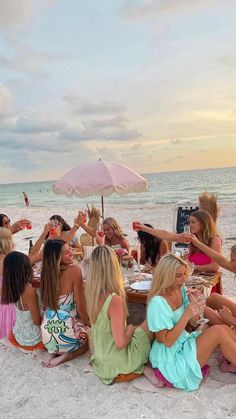 a group of women sitting on top of a sandy beach next to the ocean at sunset