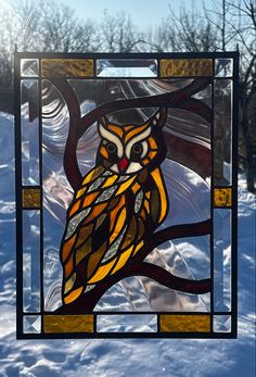 a stained glass owl sitting on top of a tree branch in front of snow covered ground