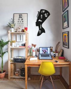 a laptop computer sitting on top of a wooden desk next to a yellow chair and potted plant