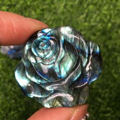 a hand holding a glass rose in it's left hand on some green grass