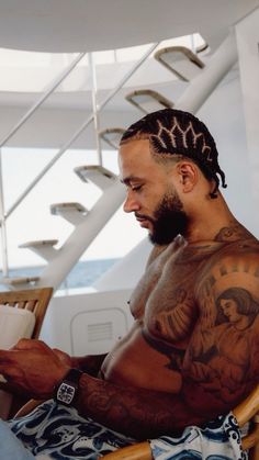 a man sitting in a chair with tattoos on his arms and chest reading a book