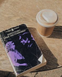 a book sitting on top of a wooden table next to a cup of coffee