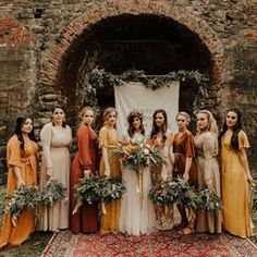 a group of women standing next to each other in front of a stone wall with greenery