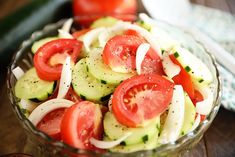 a glass bowl filled with cucumber and tomatoes on top of a wooden table