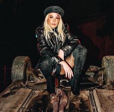 a woman sitting on top of a car with her legs crossed and wearing leather pants