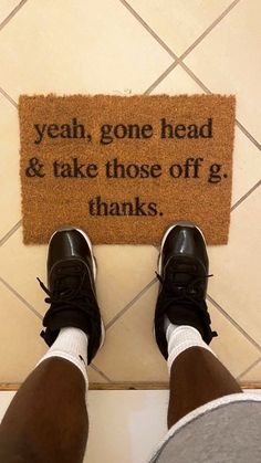 a person standing in front of a door mat that says yeah, gone head & take those off g thanks