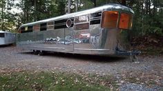 a silver trailer parked on top of a gravel road in the woods next to trees