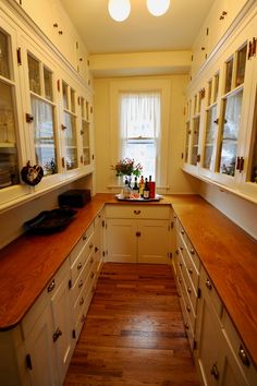 a narrow kitchen with white cabinets and wood counter tops, along with hardwood flooring