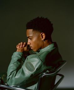 a young man sitting in a chair with his hands on his chin and looking off to the side