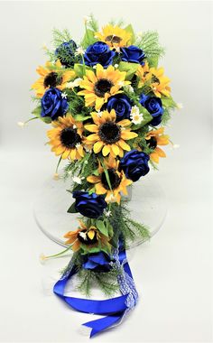 a bouquet of sunflowers and blue roses in a clear glass vase with ribbon