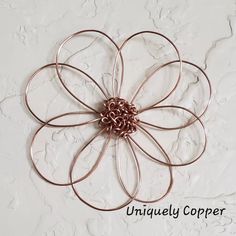 a large metal flower on a white wall with copper colored wire attached to the petals