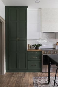 a kitchen with dark green cabinets and white walls, hardwood flooring and an area rug