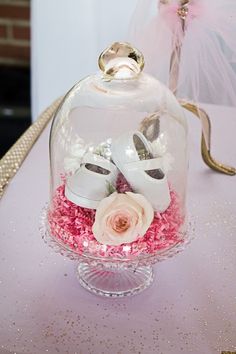 there is a glass dome with shoes and flowers in it on top of a table