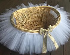 a wicker basket with white tulle and a gold bow on the bottom sitting on a wooden floor