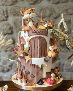 a three tiered cake decorated with fall leaves and animals is on a wooden table