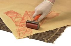 a person is using a paint roller to decorate fabric with orange designs on it and brown paper