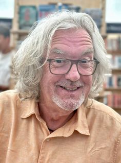 an older man with glasses is smiling for the camera in front of bookshelves