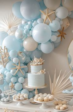 a table topped with blue and white desserts next to a wall covered in balloons